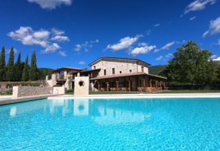 Zwembad en stenen huis bij Camping Il Collaccio, een vakantiepark in Umbrië, Italië, onder blauwe lucht.