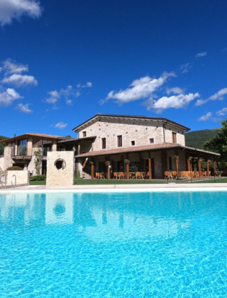 Vista della piscina e della villa in pietra al Camping Il Collaccio, parco vacanze in Umbria, Italia.