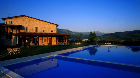 Casale in pietra con terrazza e grande piscina al tramonto tra le colline verdi dell’Umbria, Italia.