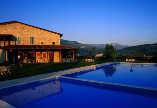 Casa de piedra con terraza y gran piscina al atardecer en las colinas pintorescas de Umbría, Italia.