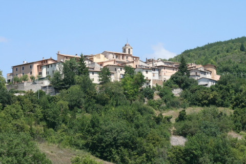View of a hilltop village surrounded by lush greenery at Camping Il Collaccio, Umbria, Italy, on a sunny day.