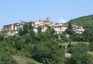 View of a hilltop village surrounded by lush greenery at Camping Il Collaccio, Umbria, Italy, on a sunny day.