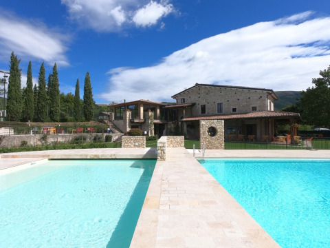 Vista de la piscina y casa de piedra en Camping Il Collaccio, un parque vacacional en Umbría, Italia.