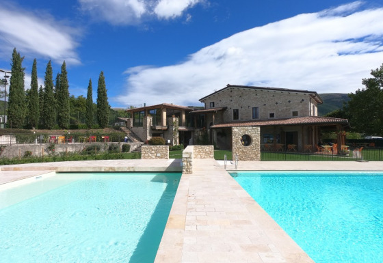 Vista sulla piscina e casa in pietra al Camping Il Collaccio, villaggio vacanze in Umbria, Italia.