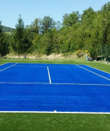 Campo da tennis blu circondato da colline e alberi verdi al Camping Il Collaccio, Umbria, Italia.