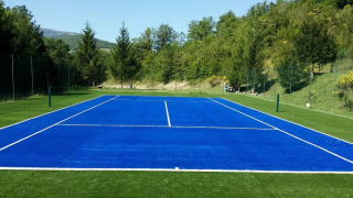 Campo da tennis blu circondato da colline e alberi verdi al Camping Il Collaccio, Umbria, Italia.