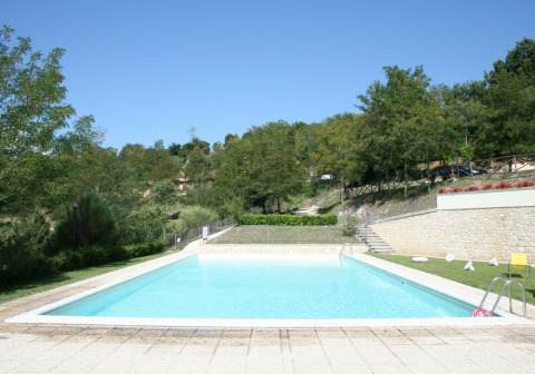 Outdoor swimming pool at Camping Il Collaccio holiday park in Umbria, Italy, surrounded by lush greenery.