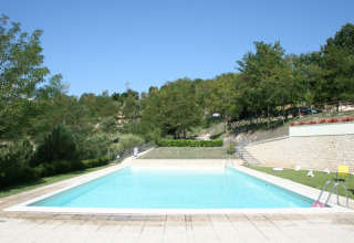 Outdoor swimming pool at Camping Il Collaccio holiday park in Umbria, Italy, surrounded by lush greenery.