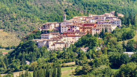Veduta di Preci, borgo collinare in Umbria, Italia, circondato da boschi rigogliosi e verdi colline.