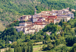 View of Preci, a hilltop town in Umbria, Italy, surrounded by lush green hills and dense forest.