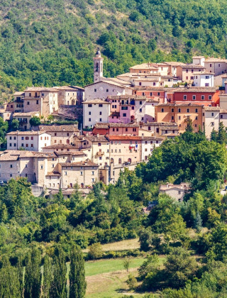 Veduta di Preci, borgo collinare in Umbria, Italia, circondato da boschi rigogliosi e verdi colline.