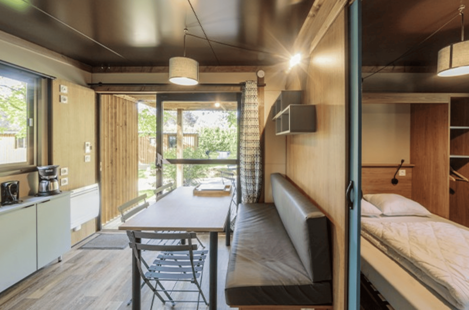 Modern interieur van Chalet Evasion op Camping de Lyon, Frankrijk, met eettafel, keuken en bed.