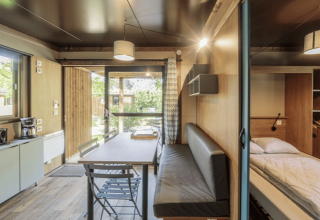 Interior moderno del Chalet Evasion en Camping de Lyon, Francia, con mesa, cocina y cama visibles.