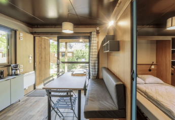 Innenraum von Chalet Evasion auf Camping de Lyon in Frankreich, mit Küche, Tisch, Sofa und Bett.