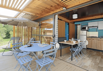 Lyst og moderne udendørs spiseområde og køkken i Chalet Evasion på Camping de Lyon, omgivet af natur.