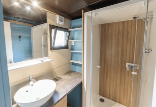 Baño moderno en Chalet Evasion, Camping de Lyon, Francia, con ducha de vidrio, lavabo y estantes azules.