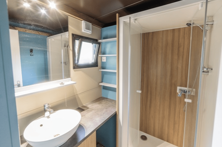 Baño moderno en Chalet Evasion, Camping de Lyon, Francia, con ducha de vidrio, lavabo y estantes azules.
