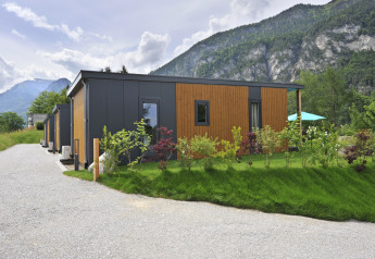 Mountain Lodges con moderne mini case immerse nel verde e montagne sullo sfondo sotto un cielo nuvoloso.