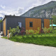 Et billede af Mountain Lodges, små moderne hytter omgivet af bjerge og grøn natur under en skyet himmel.