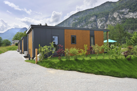 Mountain Lodges avec des petites cabanes modernes entourées de verdure et de montagnes sous un ciel nuageux.