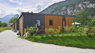 Mountain Lodges con moderne mini case immerse nel verde e montagne sullo sfondo sotto un cielo nuvoloso.