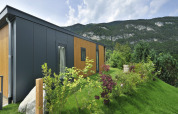 Lodge moderno de montaña con fachada de madera y metal en colina verde, con montañas al fondo.