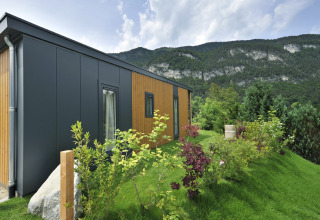 Lodge moderno de montaña con fachada de madera y metal en colina verde, con montañas al fondo.