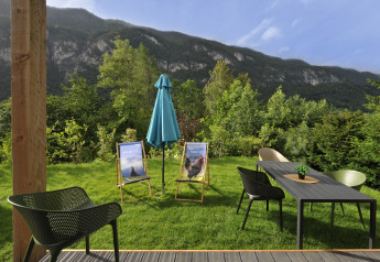 Buitenzitplaats bij Mountain Lodges met stoelen, tafel, parasol en zicht op bergen en bos.