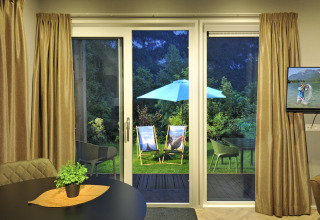 View from Mountain Lodges living room to garden with loungers and umbrella through large glass doors at dusk.