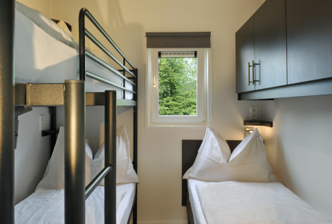 Habitación con litera y cama individual en Mountain Lodges, decoración clara y ventana al bosque verde.