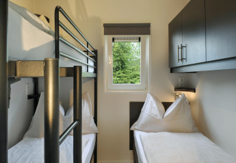 Kamer met stapelbed en eenpersoonsbed in Mountain Lodges, licht interieur, raam met uitzicht op bos.