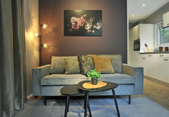 Modern living room in Mountain Lodges with a grey sofa, stylish lights, plant decor, art, and kitchen view.