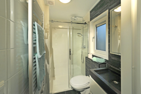 Baño moderno en Mountain Lodges con ducha de vidrio, lavabo negro, toallas y ventana esmerilada.