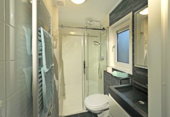 Baño moderno en Mountain Lodges con ducha de vidrio, lavabo negro, toallas y ventana esmerilada.