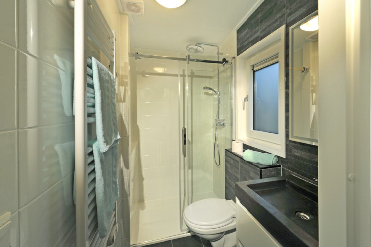 Modernes Bad im Mountain Lodges mit Duschkabine, schwarzem Waschbecken und Handtüchern am Heizkörper.