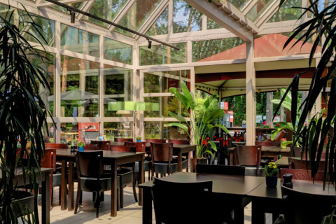 Luminoso comedor con ventanales grandes y plantas en Camping Kempen, parque vacacional de Amberes, Bélgica.