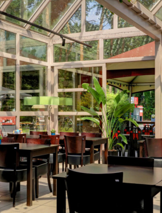 Lichte eetruimte met grote ramen en veel planten bij Camping Kempen, vakantiepark in Antwerpen, België.