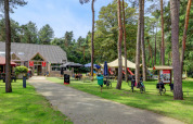 Campingplads med café, cykler og legeplads omgivet af træer i Kempen, Antwerpen, Belgien.