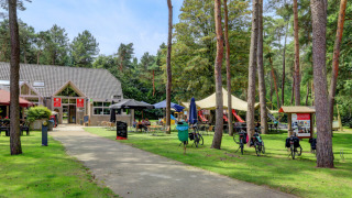 Campingplads med café, cykler og legeplads omgivet af træer i Kempen, Antwerpen, Belgien.