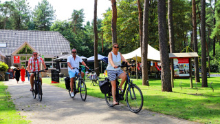 People cycling through a green area at Camping Kempen holiday park in Antwerp, Belgium, surrounded by trees.