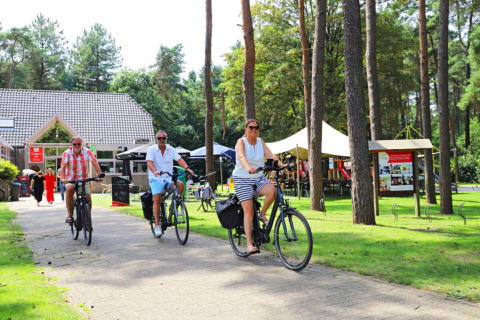 Personas montando bicicletas por una zona verde del Camping Kempen, un parque vacacional en Amberes, Bélgica.