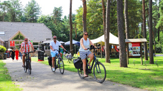 Personas montando bicicletas por una zona verde del Camping Kempen, un parque vacacional en Amberes, Bélgica.