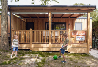 Twee kinderen spelen met een bal voor SunLodge Katsura in hu Park Albatros Village, Italië, houten lodge.