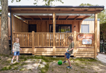 Twee kinderen spelen met een bal voor SunLodge Katsura in hu Park Albatros Village, Italië, houten lodge.