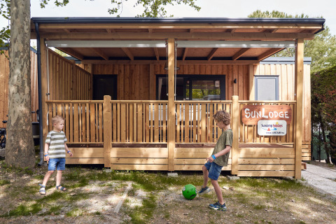 To børn leger med en bold foran SunLodge Katsura ved hu Park Albatros Village, Italien, en træhytte.