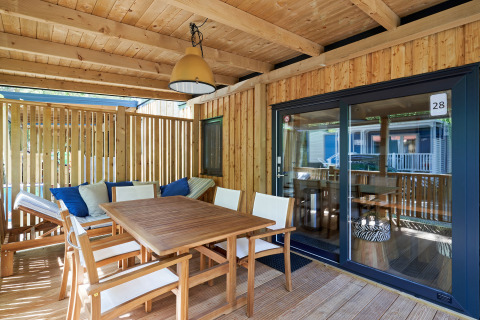 Zonnig houten terras aan SunLodge Katsura met eettafel, stoelen en bank met kussens onder dak.