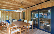 Zonnig houten terras aan SunLodge Katsura met eettafel, stoelen en bank met kussens onder dak.