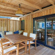 Solrig træterrasse på SunLodge Katsura med spisebord, stole og bænk med puder under overdækning.