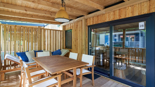 Terrasse en bois ensoleillée à SunLodge Katsura avec table à manger, chaises et banc avec coussins.
