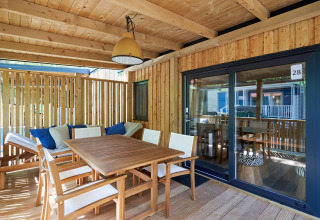 Terrasse en bois ensoleillée à SunLodge Katsura avec table à manger, chaises et banc avec coussins.